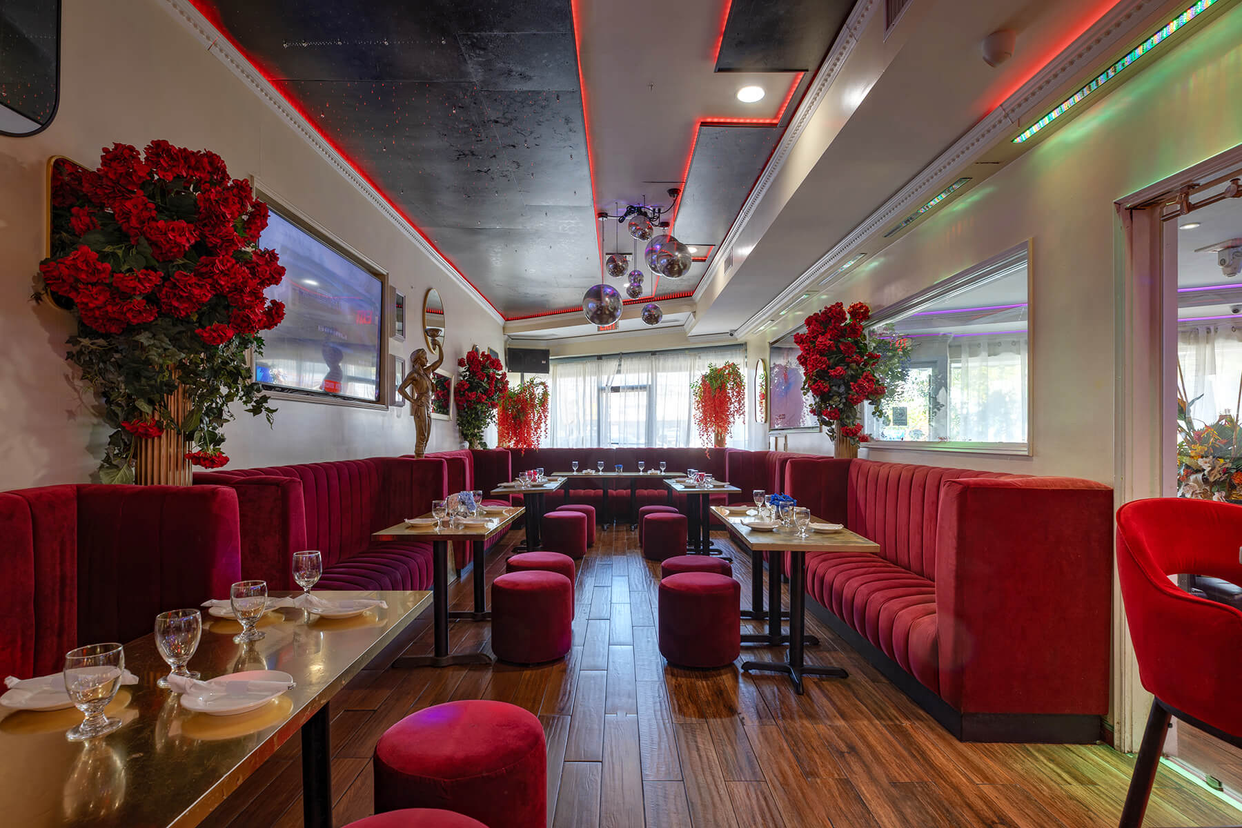 Upscale lounge with red velvet seating, small tables set with glassware, wooden floors, and red floral arrangements.