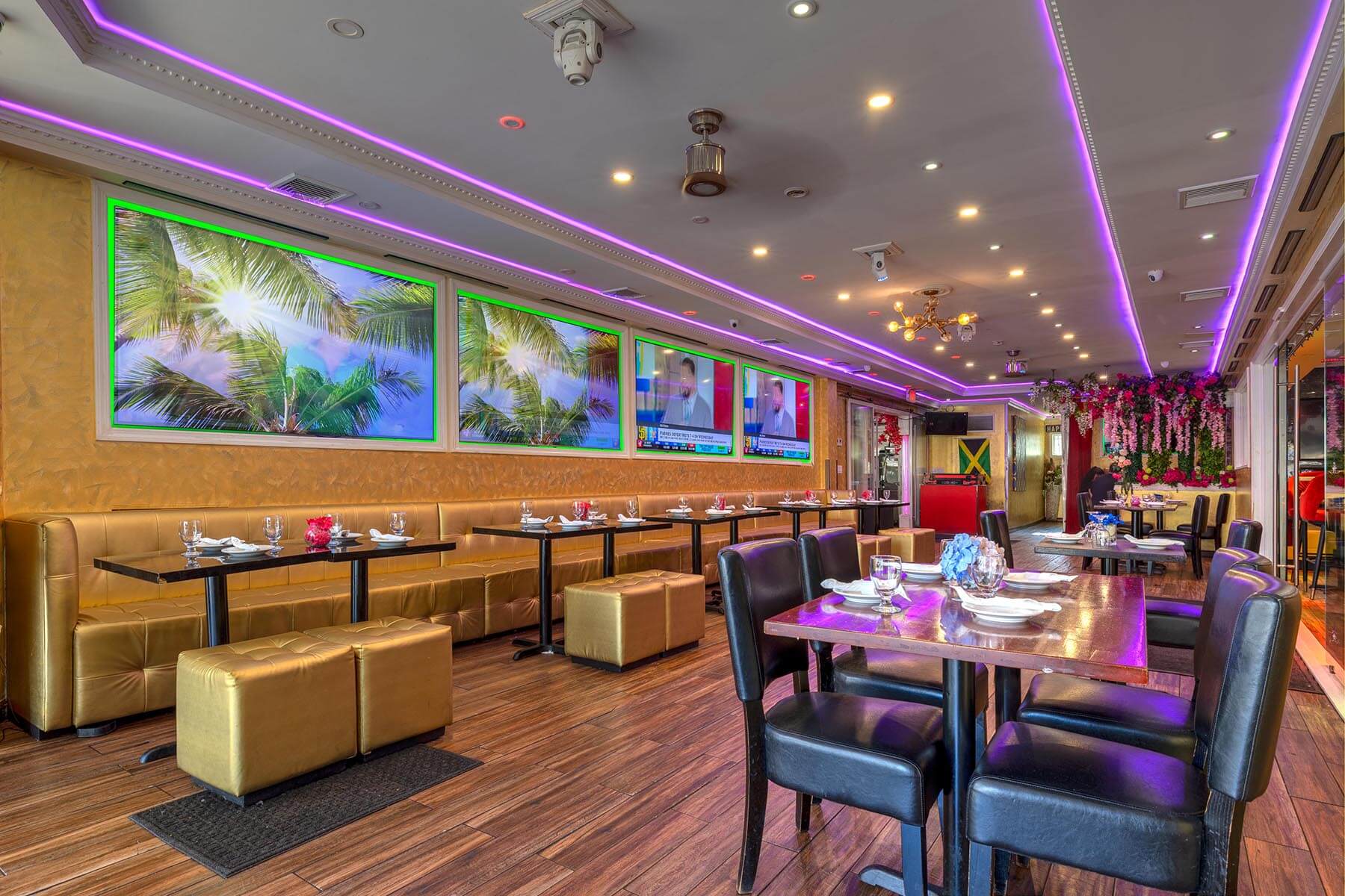 Modern restaurant interior with purple LED ceiling lights, gold seating along the wall, black chairs, and tables set with white plates and glasses.